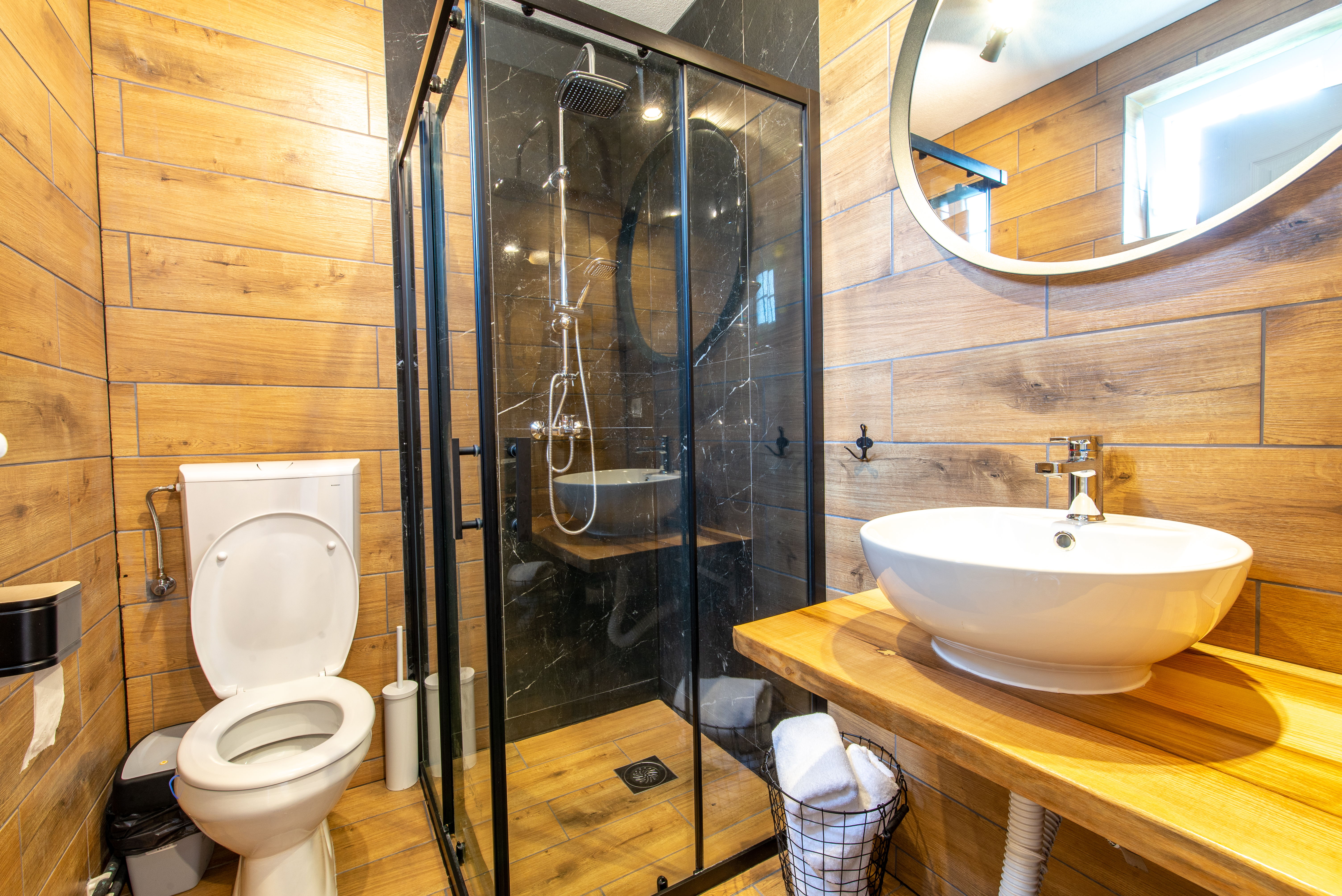 Warm bathroom featuring custom walk-in shower with matte black framed glass, wood-tile accents, and floating vanity.